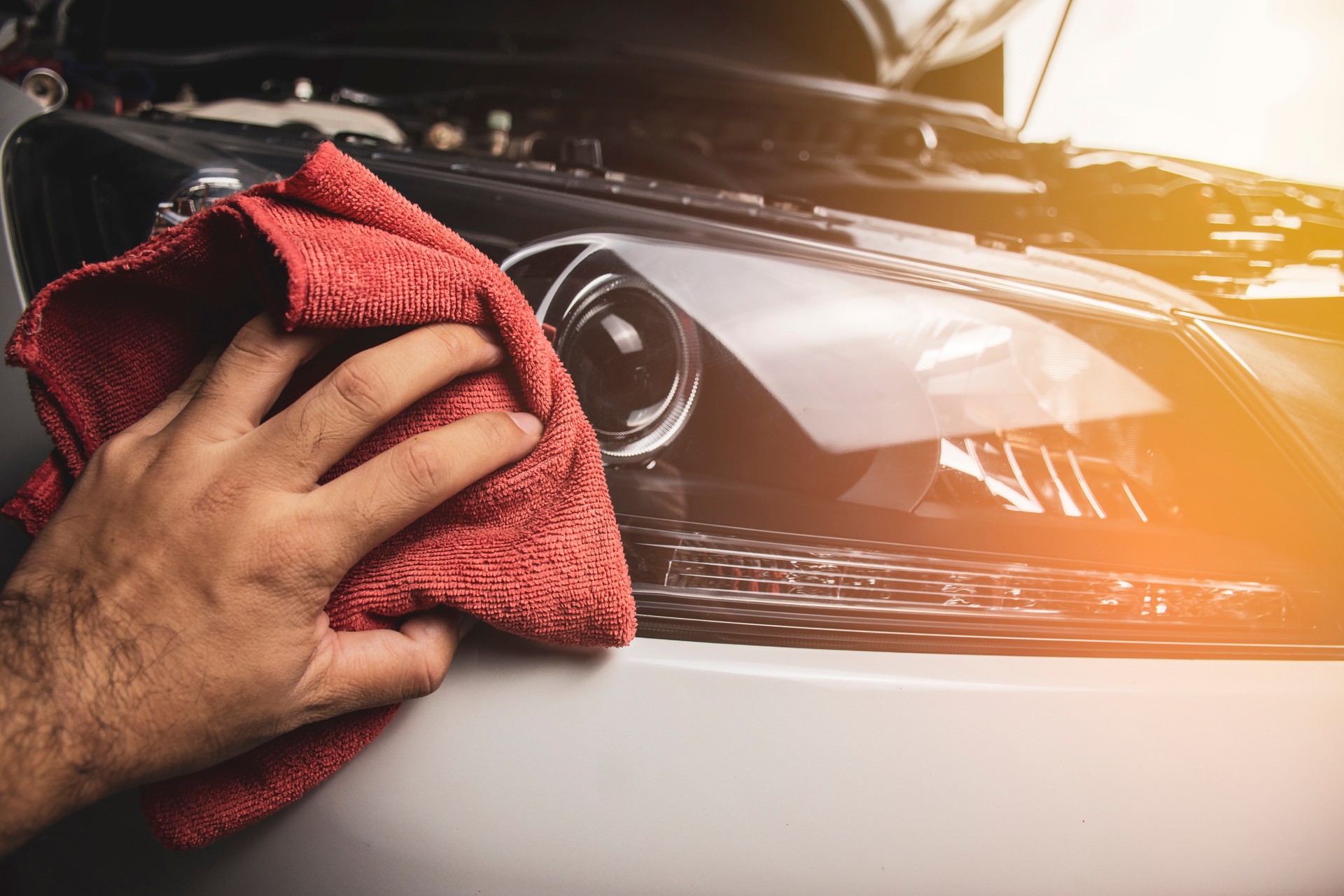 Hand is cleaning car headlight with a using red microfiber cloth.